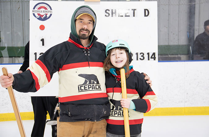 Two people, father and son, smile for a picture while curling