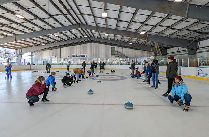 Many people on the ice on the side lines while curling